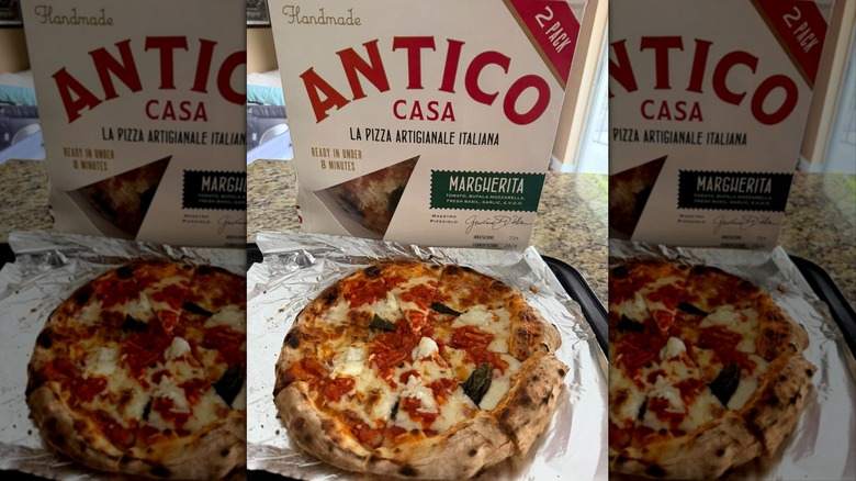 A box of Antico frozen pizza is propped up behind a baked margherita pie.