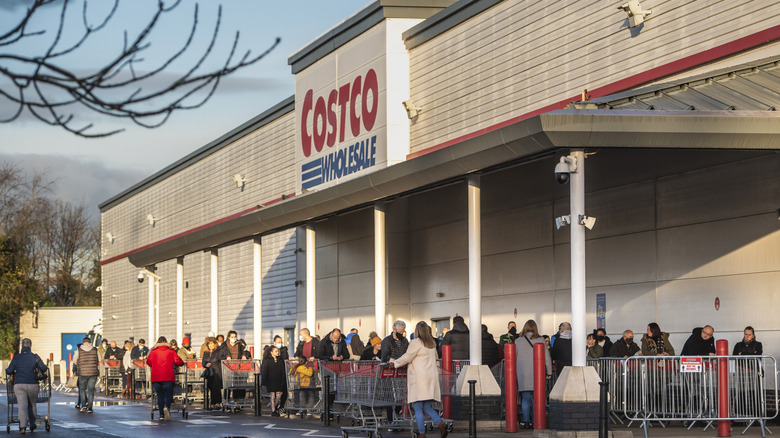 Customers lined up outside of a Costco warehouse waiting to be allowed inside