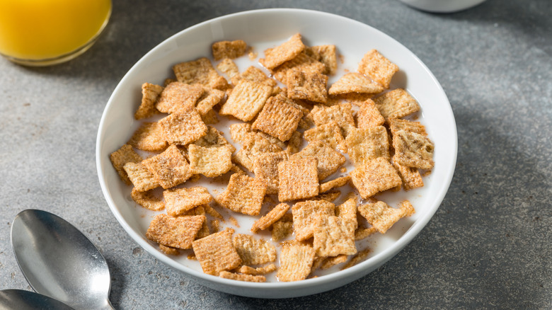 Bowl of cereal with a spoon next to a glass of orange juice