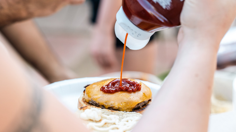 Close-up shot of a person squirting ketchup onto a cheeseburger