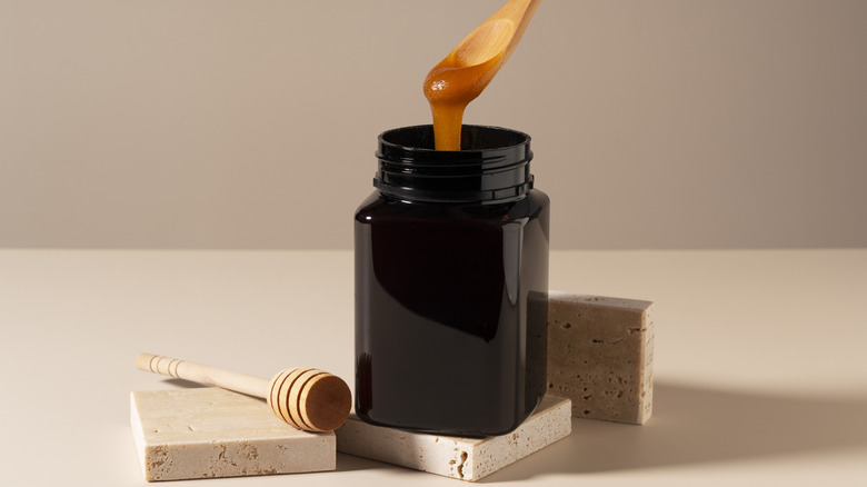 Manuka honey in a dark jar with a wooden spoon