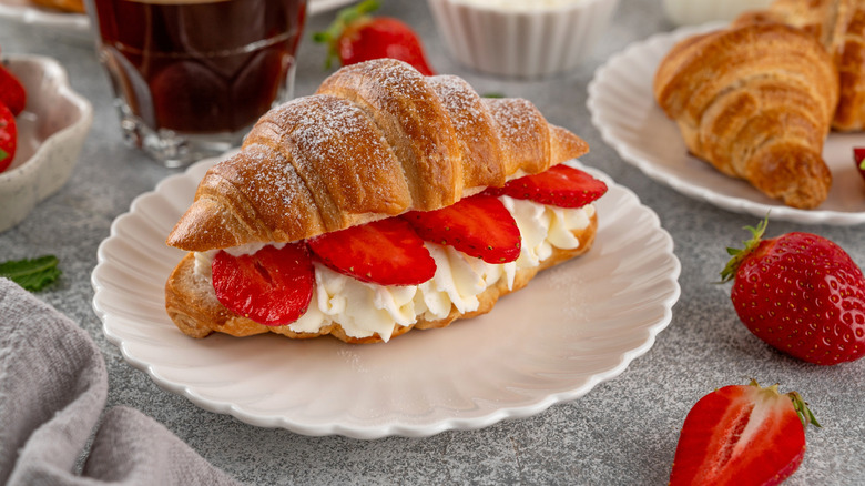 A croissant filled with whipped cream and sliced strawberries on a white plate