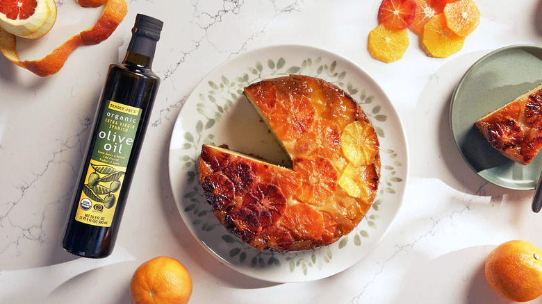 Bottle of Trader Joe's Organic Extra Virgin Spanish Olive Oil next to plate of cake with orange slices on top on marble counter
