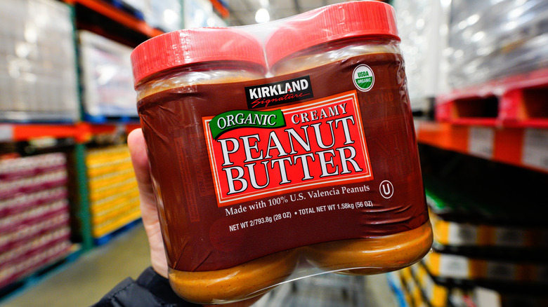 Hand holding two pack of peanut butter in Costco aisle