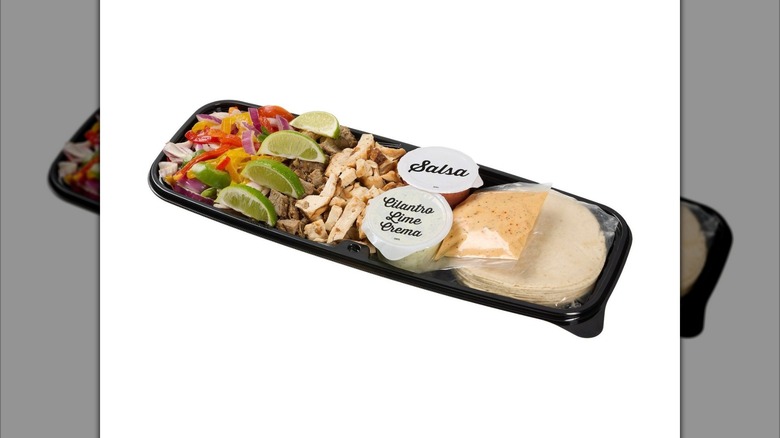 Kirkland Signature Beef and Chicken Fajita Kit with tortillas, meat, limes, and sauce cups on white background