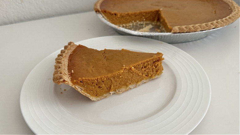 Piece of Costco pumpkin pie with large pie in the background