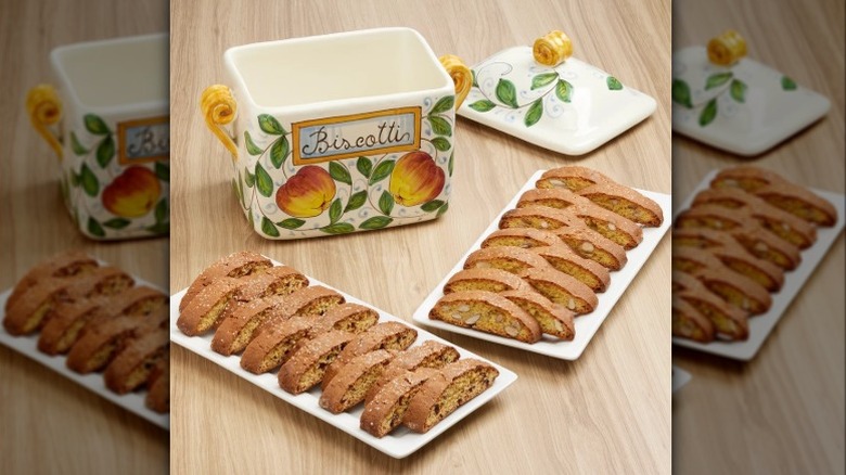 A hand painted ceramic Belli biscotti cookie jar, two plates of biscotti, all sitting on a wooden looking table or counter.
