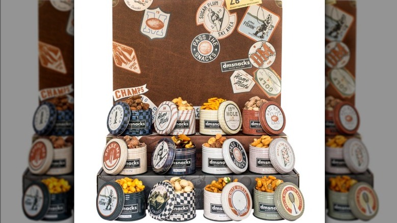 A 12-pack variety of Damn Man bar snacks in decorative vintage tins showing their contents of nuts, popcorn, trail mix, and more.