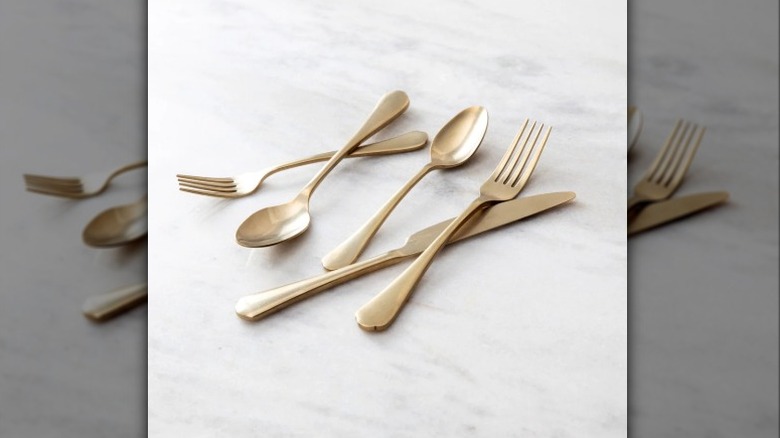 A single place setting of Fortessa Ellsie antiqued champagne flatware on a neutral gray countertop.