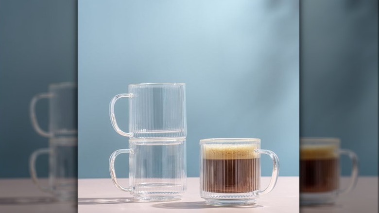 JoyJolt stackable glass mugs, two empty and stacked and one with coffee, on a neutral countertop with a gray blue background.