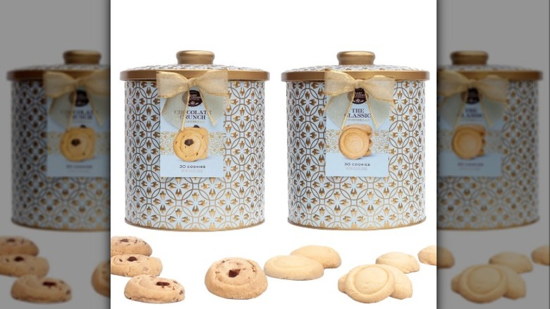 Two embossed tins of Mary Macleod's shortbread cookies with scattered shortbread in front of them on a white background.