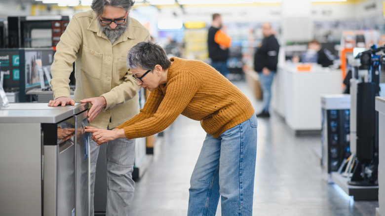 A couple of people shopping for a dishwasher with other appliances blurred behind them
