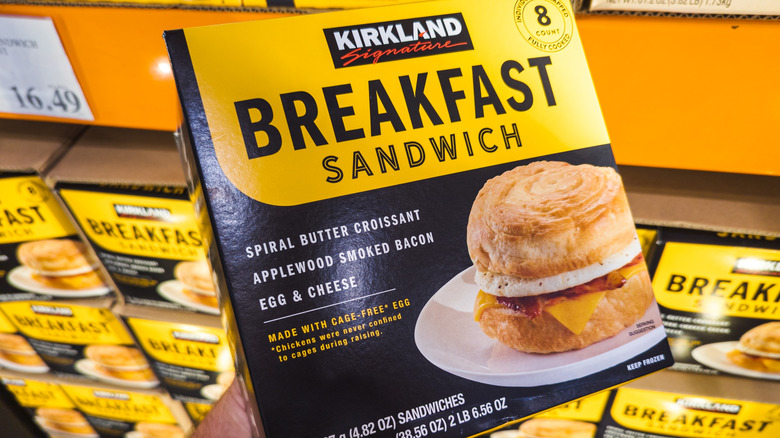 Kirkland Signature frozen breakfast sandwich, being held in front of multiple product boxes