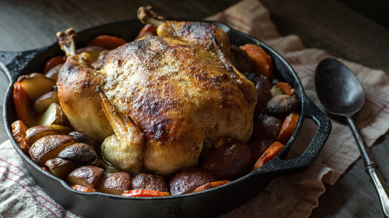 A whole roasted chicken with potatoes in cast iron skillet.