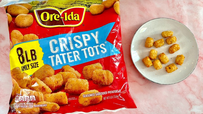 Ore-Ida Crispy Tater Tots on white plate next to bag, on pink marble surface