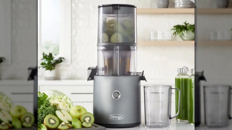 Omega Effortless Batch Juicer on kitchen counter next to glasses and cut fruits including kiwi and apples