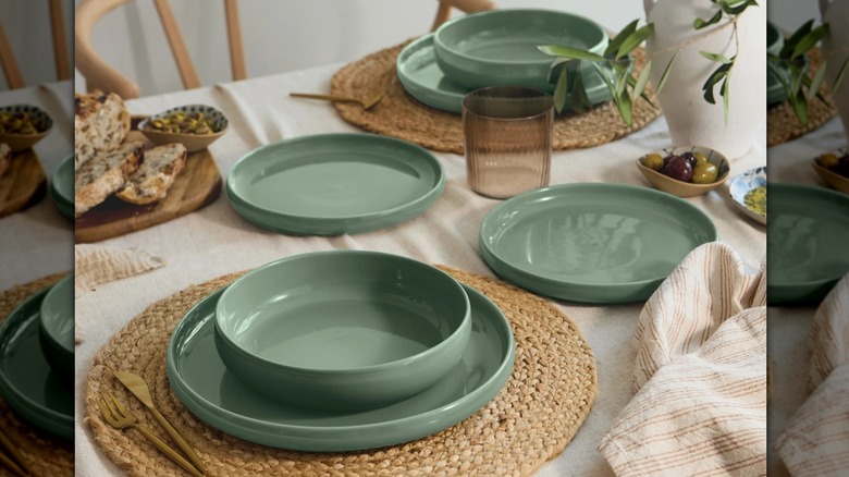 Safdie Alma Dinnerware plates and bowls in green color on table set with woven placemats and potted plants