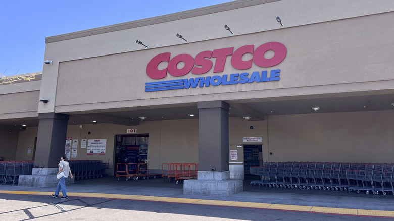 Exterior of a Costco warehouse with a woman walking in front of the building