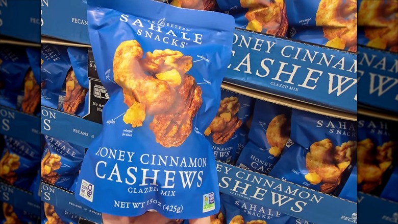 A person holding a blue bag of Sahale Snacks Honey Cinnamon Cashews Glazed Mix in front of a Costco display