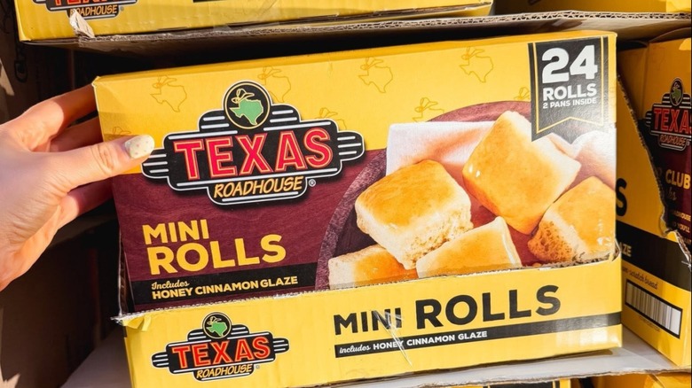 A woman's hand grabbing a yellow box of Texas Roadhouse Mini Rolls from a Costco shelf