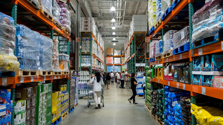 The view down an aisle at Costco with no specifically brands obvious and people are shopping in the background