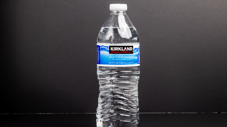 A plastic bottle of Kirkland Signature purified water on a gray background