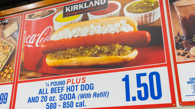 A menu board showing a Costco hot dog on a bun with relish and onions next to a drink and other condiments. The board list the description plus the price of $1.50