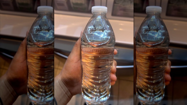 A person holding a label-less bottle of Kirkland Signature water from Costco