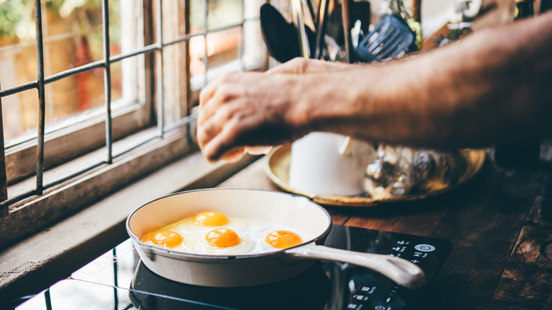 A person cracking eggs into a pan