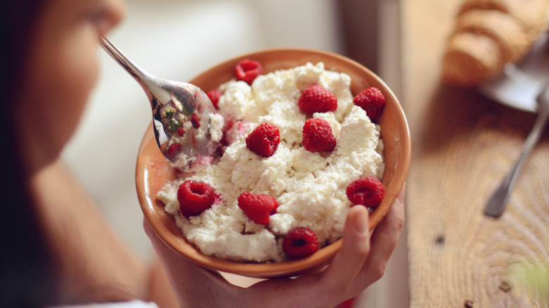 A person eating a bowl of cottage cheese with raspberries