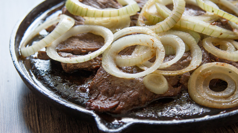 Cooked beef in a pan topped with sliced onions