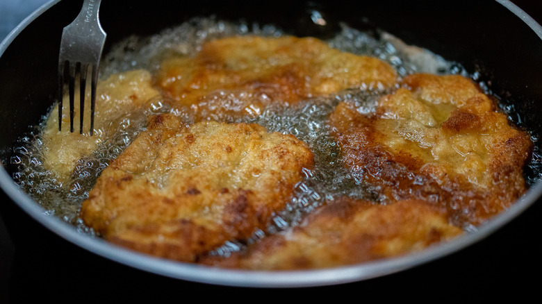 Breaded beef cutlets frying in bubbly oil with fork