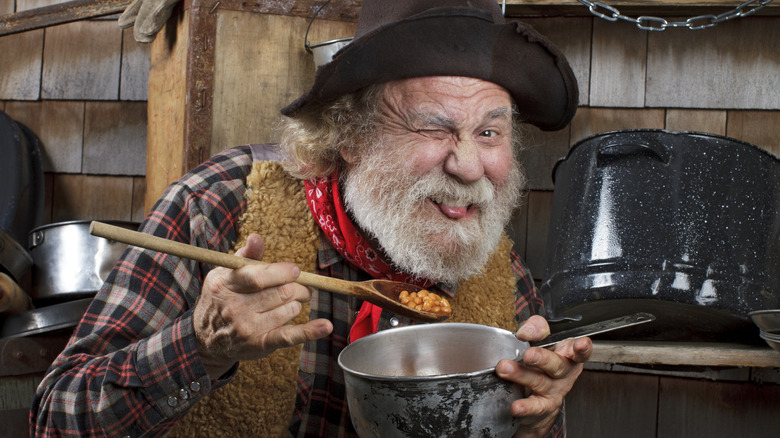 Chuck wagon cook with pot and spoonful of beans making a funny face