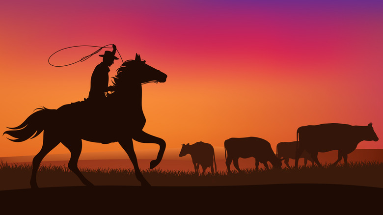 Silhouette of a cowboy on a horse with cattle against sunet