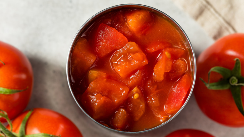 Overhead angle of an open can of diced tomatoes, with fresh tomatoes surrounding it