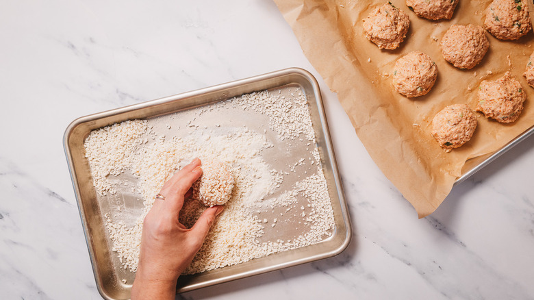 Rolling jalapeno bites in breadcrumbs on baking sheet
