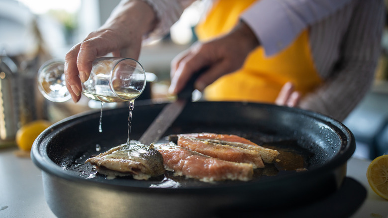 Home cook pouring beer over a pan of salmon