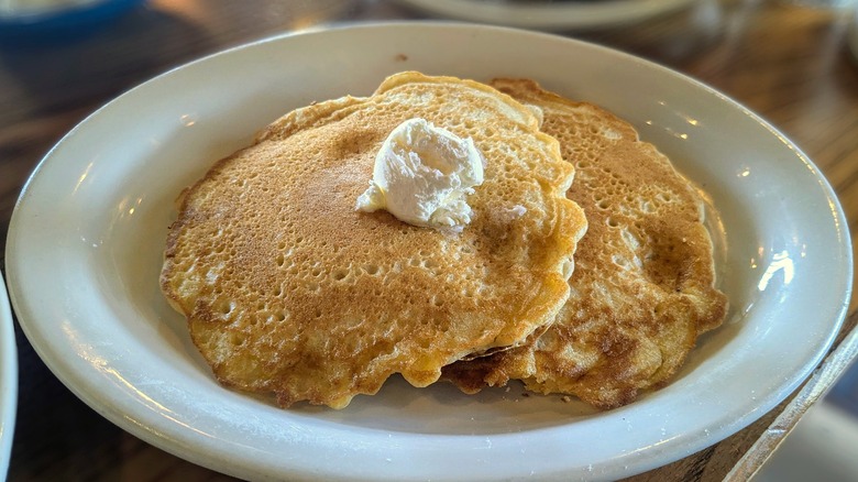 Two thin buttermilk pancakes with a small scoop of butter on top on a white oval plate