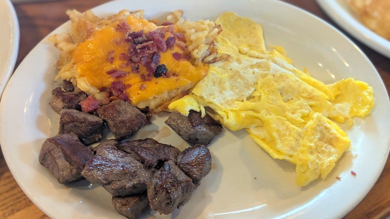 Steak tips, loaded hashbrowns, and scrambled eggs on a white plate