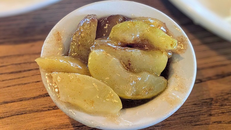 Slices of cooked apples covered in cinnamon-and-sugar jelly in a tiny white bowl