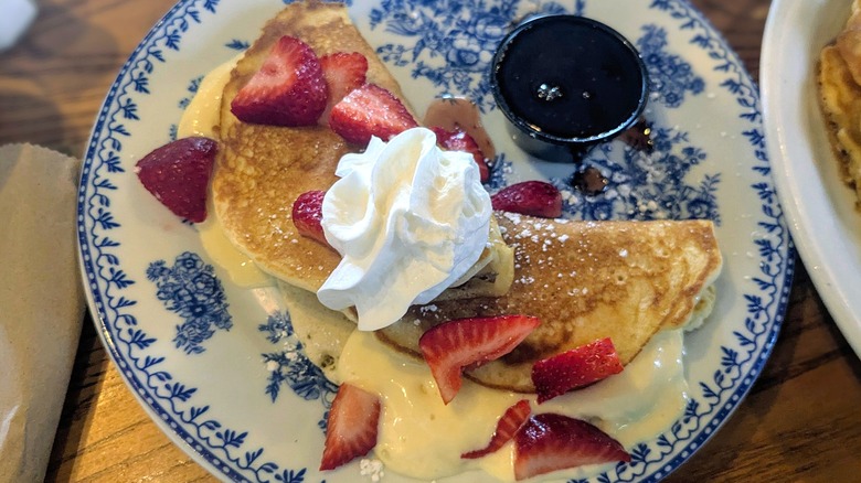 Folded pancakes stuffed with cream cheese frosting and topped with fresh strawberries and whipped cream on an ornate blue and white plate