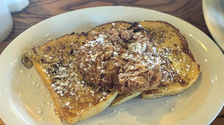 French toast covered in powdered sugar with a piece of fried chicken on top on a white oval plate