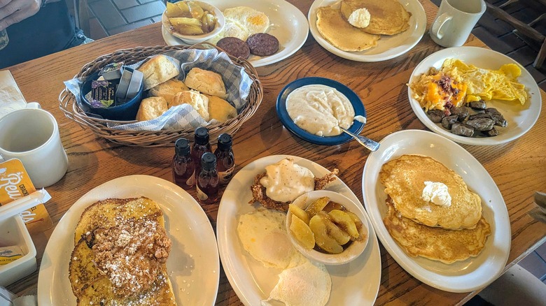 Various plates of breakfast food on a brown, wood table in a Cracker Barrel restaurant