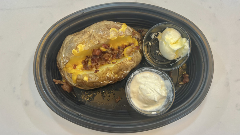 Cracker Barrel loaded baked potato in a to-go container with butter and sour cream on the side
