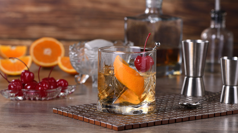 Old fashioned cocktail with cherries, oranges, bar tools