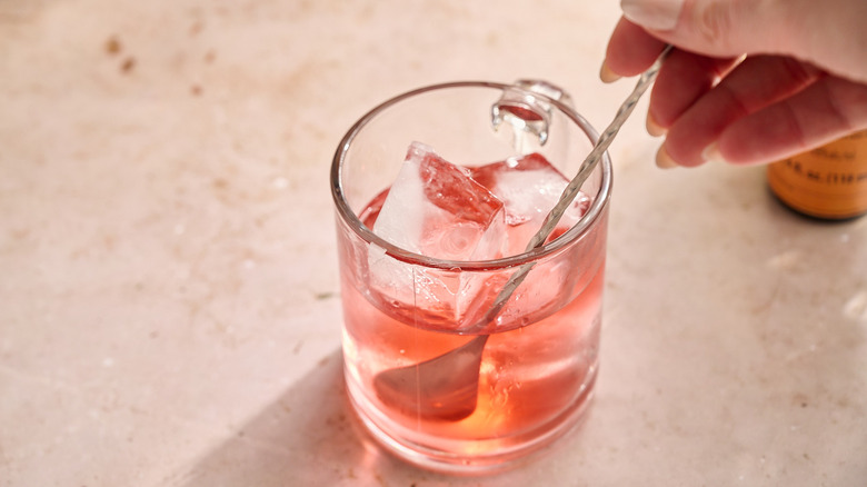 stirring cranberry and gin in a glass