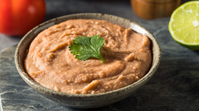Bowl of creamy refried beans with tomato and lime