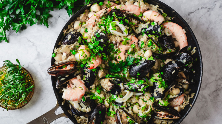Pan of seafood risotto surrounded by herbs