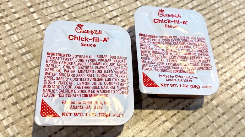 Two white packets of Chick-fil-A sauce on beige woven surface