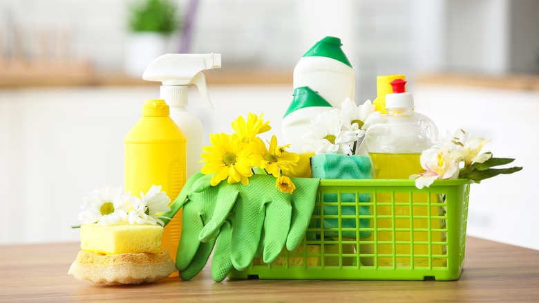 Kitchen supplies in green plastic bin including gloves, spray bottles, and sponges